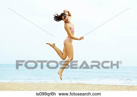 Young woman in bikini jumping on beach View Large Photo Image Stock Image - Young woman in bikini jumping on beach. Fotosearch