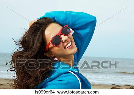 Picture - Young woman on beach with hand in hair and red sunglasses. Fotosearch
