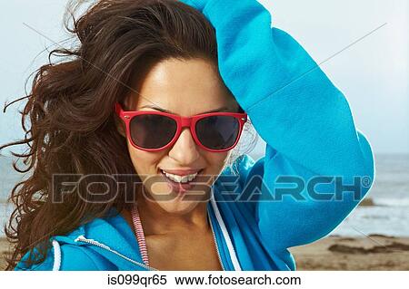 Stock Photography - Young woman on beach with hand in hair and red sunglasses. Fotosearch