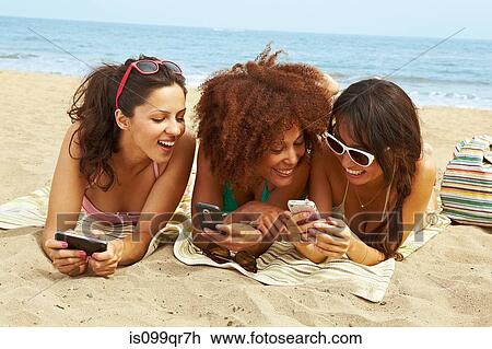 Stock Image - Young women on beach with cell phones. Fotosearch