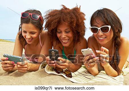 Stock Image - Young women on beach with cell phones. Fotosearch