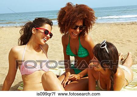 Stock Image - Young women sitting on beach. Fotosearch