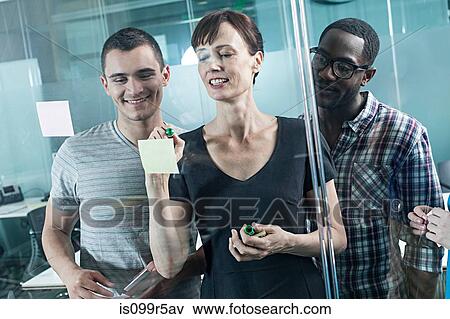 Colleagues writing on adhesive notes and sticking them to window View Large Photo Image Stock Photo - Colleagues writing on adhesive notes and sticking them to window. Fotosearch