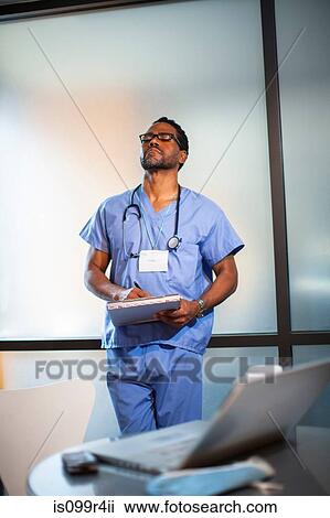 Stock Image - Doctor leaning on wall in office. Fotosearch