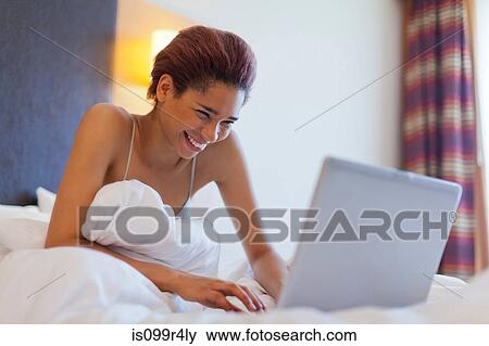 Happy young woman using laptop in bed View Large Photo Image Stock Photo - Happy young woman using laptop in bed. Fotosearch