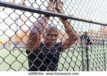 Picture - Man leaning on chain link fence. Fotosearch