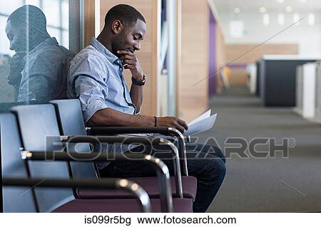 Stock Image - Man sitting on chair reading document. Fotosearch