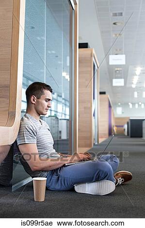 Stock Image - Man sitting on floor using laptop. Fotosearch