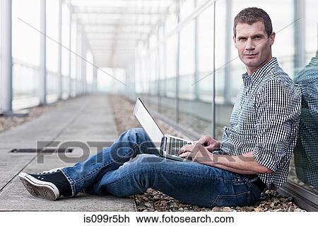 Stock Image - Man sitting on floor using laptop. Fotosearch