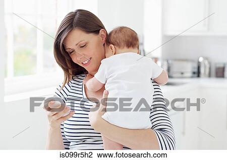 Mother holding baby and using cellphone View Large Photo Image Stock Image - Mother holding baby and using cellphone. Fotosearch