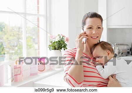 Mother holding baby and using cellphone View Large Photo Image Stock Photo - Mother holding baby and using cellphone. Fotosearch