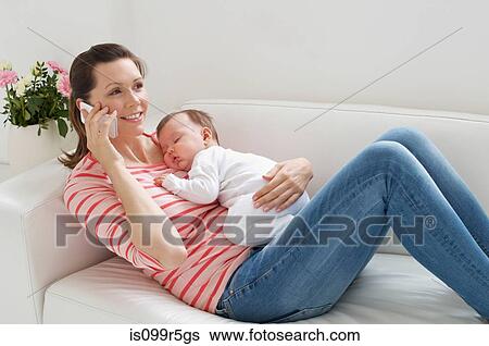 Mother on sofa with baby whilst on cellphone View Large Photo Image Stock Photograph - Mother on sofa with baby whilst on cellphone. Fotosearch