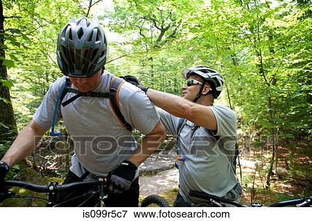 Mountain biker fixing friend's backpack View Large Photo Image Stock Photo - Mountain biker fixing friend's backpack. Fotosearch