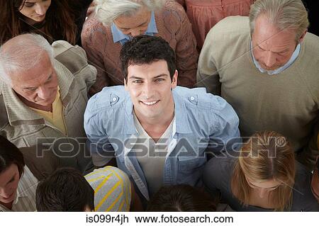 Stock Image - Portrait of man looking up at camera in group of people, high angle. Fotosearch