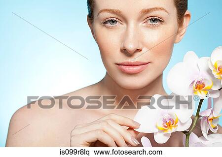 Stock Photography - Woman holding orchid, looking at camera. Fotosearch