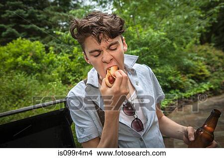 Picture - Young man eating a hotdog. Fotosearch