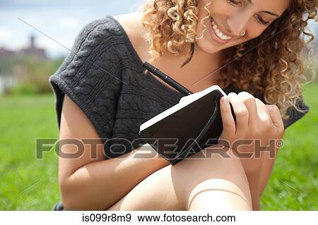 Stock Photo - Young woman in park, writing in notebook. Fotosearch