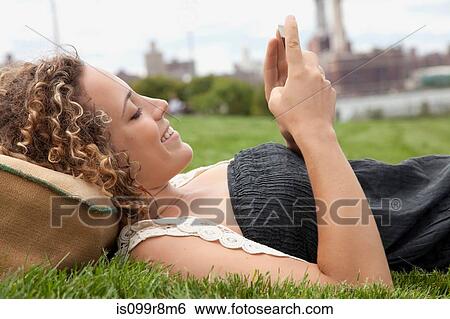 Young woman lying on grass and looking at smartphone View Large Photo Image Stock Photograph - Young woman lying on grass and looking at smartphone. Fotosearch