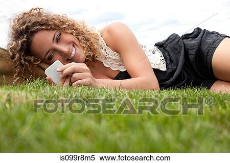 Young woman lying on grass and looking at smartphone View Large Photo Image Stock Photography - Young woman lying on grass and looking at smartphone. Fotosearch