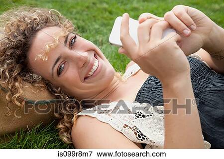 Young woman lying on grass with smartphone View Large Photo Image Stock Photo - Young woman lying on grass with smartphone. Fotosearch