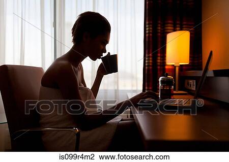 Stock Image - Young woman sitting at laptop in hotel room. Fotosearch