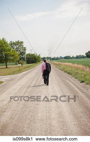 Stock Image - Businessman walking away down a dirt road. Fotosearch