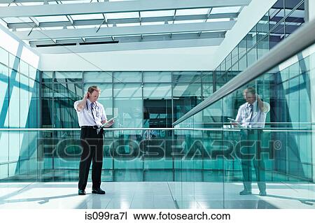 Stock Image - Doctor holding medical records in hospital corridor. Fotosearch