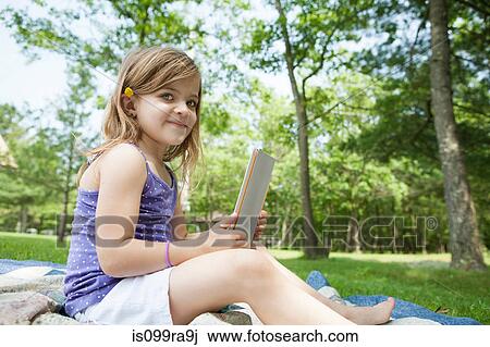 Stock Image - Girl sitting on picnic blanket with digital tablet. Fotosearch