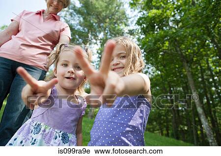 Stock Image - Girls making victory sign with grandmother in background. Fotosearch