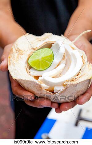 Stock Image - Person holding coconut with lime. Fotosearch