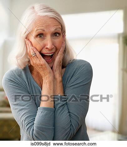 Stock Image - Senior woman gasping with mouth open, touching face. Fotosearch