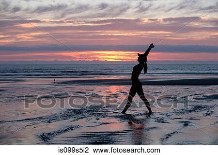Stock Image - Silhouette of young woman stretching by the sea at sunset. Fotosearch
