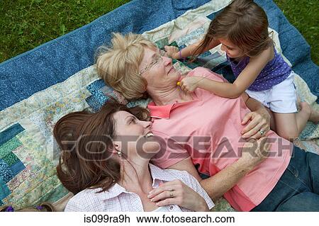 Stock Image - Three generation family lying on picnic blanket. Fotosearch