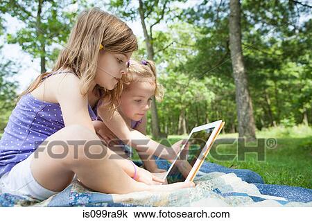 Two girls sitting on picnic blanket with digital tablet View Large Photo Image Stock Image - Two girls sitting on picnic blanket with digital tablet. Fotosearch