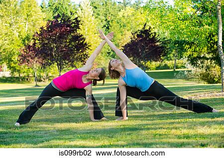 Stock Image - Two women practising yoga together in a park. Fotosearch