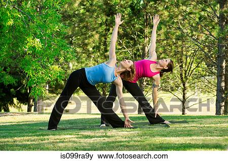 Stock Photo - Two women practising yoga together in a park. Fotosearch