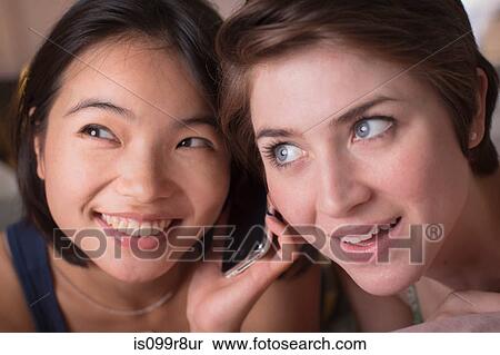 Stock Photography - Two young women listening to cellphone together. Fotosearch