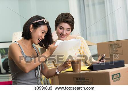 Stock Image - Two young women looking at paperwork for new apartment. Fotosearch