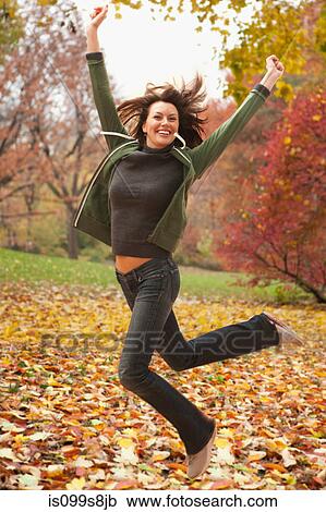 Stock Image - Woman jumping in autumn leaves. Fotosearch