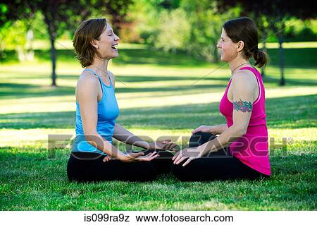 Women practising yoga in park, sitting face to face View Large Photo Image Stock Photo - Women practising yoga in park, sitting face to face. Fotosearch
