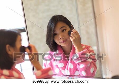 Stock Photo - Young woman applying makeup using bathroom mirror. Fotosearch