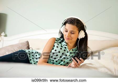 Young woman on bed wearing earphones View Large Photo Image Picture - Young woman on bed wearing earphones. Fotosearch