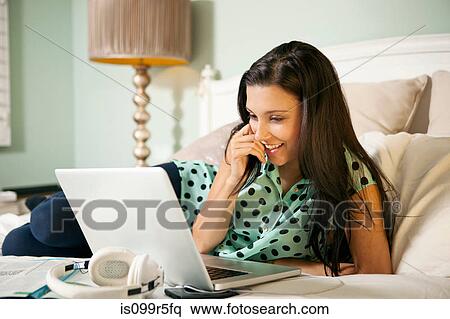 Stock Photography - Young woman on bed with laptop. Fotosearch