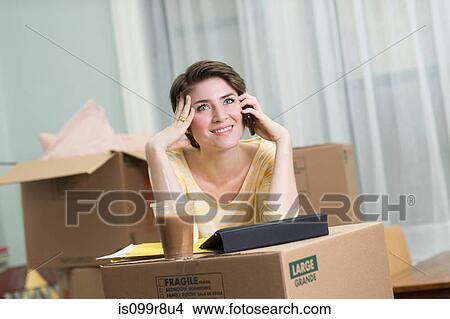 Picture - Young woman on cellphone whilst moving house. Fotosearch