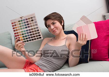 Stock Image - Young woman on sofa, looking at color swatches. Fotosearch