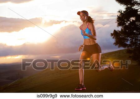 Stock Photo - Young woman running in rural setting at sunrise. Fotosearch