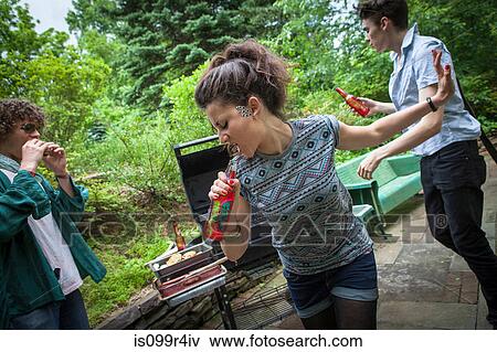 Stock Photo - Young woman singing into bottle at a backyard barbecue. Fotosearch