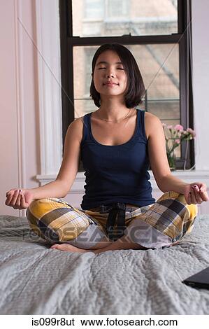 Young woman sitting on bed and meditating View Large Photo Image Stock Photograph - Young woman sitting on bed and meditating. Fotosearch