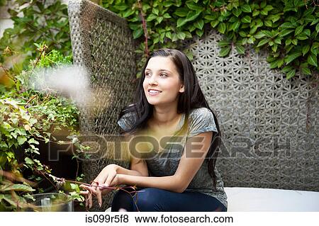 Stock Photo - Young woman sitting on bench in garden. Fotosearch