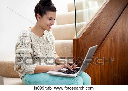 Stock Image - Young woman sitting on stairs using laptop. Fotosearch